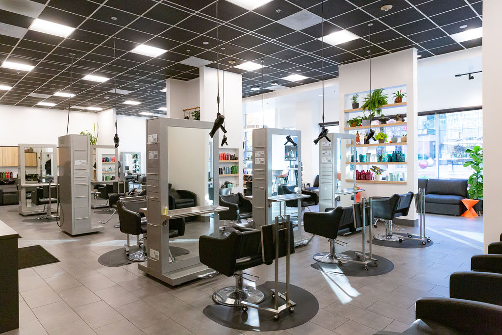 Modern hair salon interior with multiple styling stations, black chairs, large mirrors, shelves of hair products, and bright natural light from large windows. - Atelier Studio, San Jose, CA