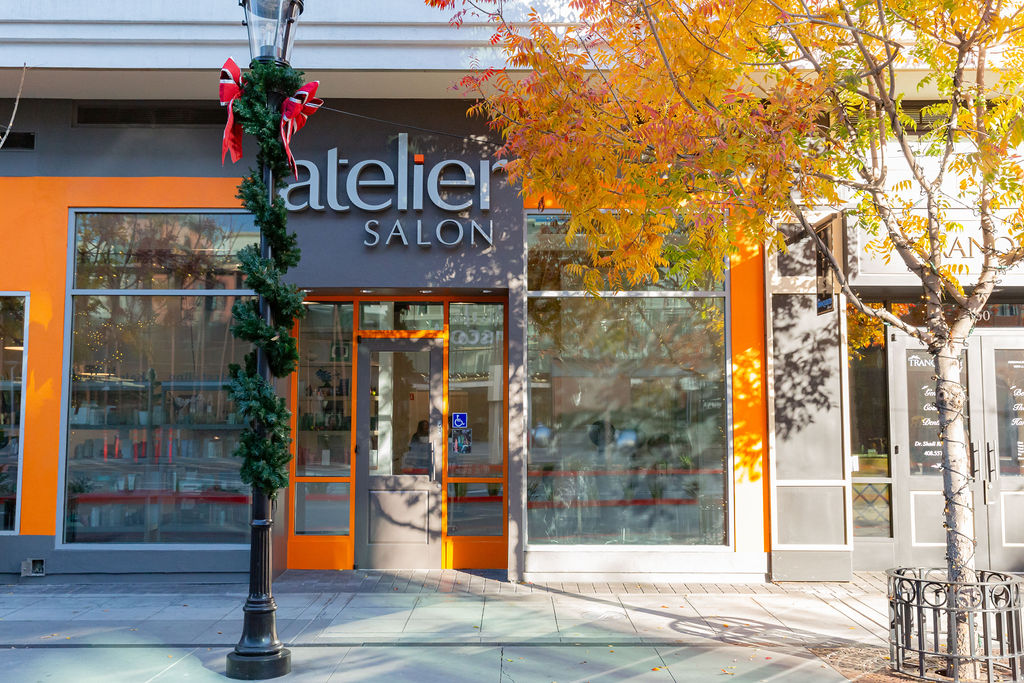 Atelier Salon storefront with large windows, orange trim, and a sign above the entrance; a decorated streetlamp and autumn tree are in front. - Atelier Studio, San Jose, CA